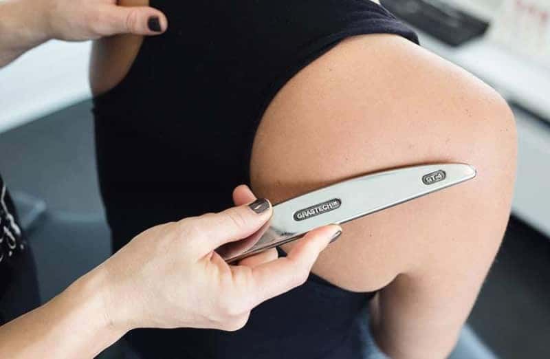 Chiropractor performing Graston on exposed patient's shoulder